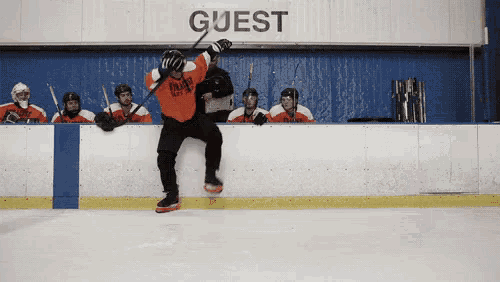a hockey player is jumping in the air in front of a wall that says guest