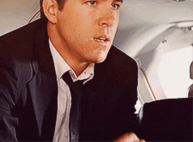 A man in a suit leans forward in disbelief on an airplane.