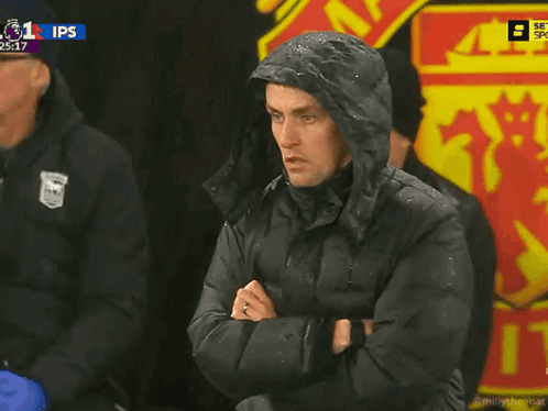 a man wearing a hooded jacket stands in front of a man united logo