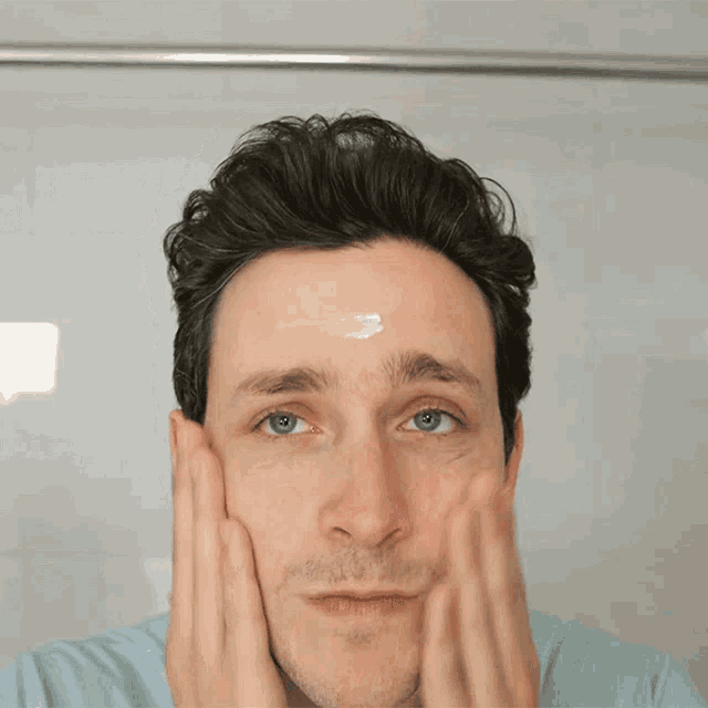 a man is applying cream to his forehead while looking in the mirror