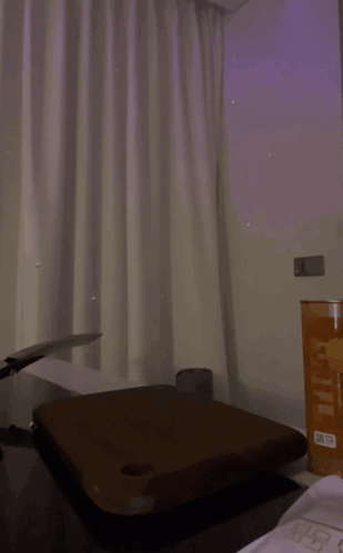 A quiet room with curtains, a table, and a bottle is shown from afar.