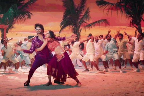 A large dance ensemble performs on a bright tropical film set.