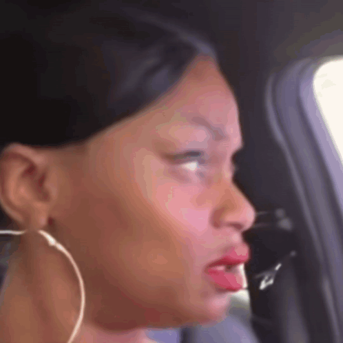 A woman in a car looks sideways with a speechless, confused expression.