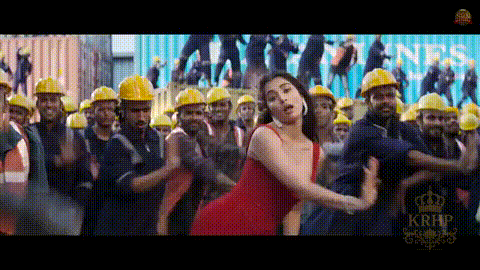 a woman in a red dress is dancing in front of a large group of construction workers wearing hard hats .