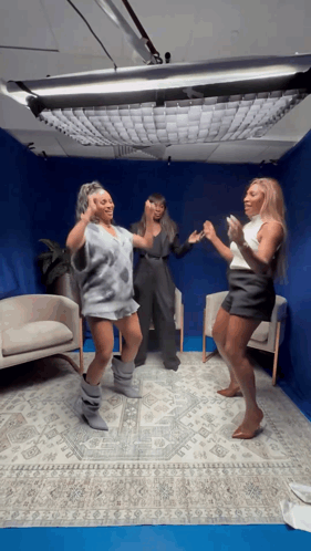 three women are dancing in a room with a blue ceiling .