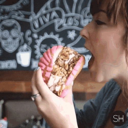 a woman eating a donut in front of a blackboard that says viva los
