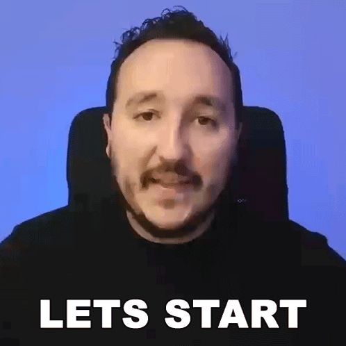 a man with a mustache is sitting in a chair with the words let 's start written on the screen behind him .