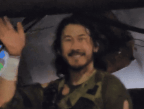 a man with long hair and a beard is smiling and waving his hand