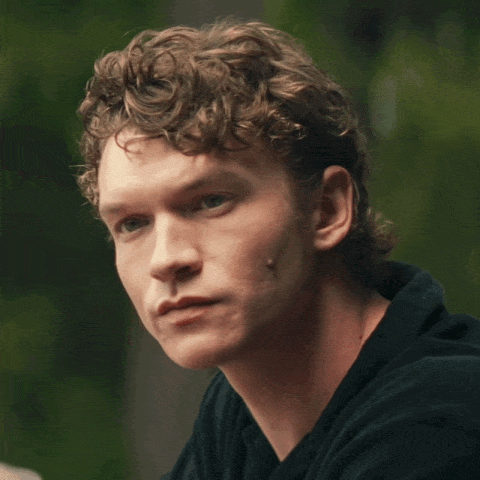 a close up of a man 's face with curly hair and a black shirt