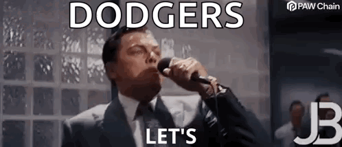 a man in a suit and tie is singing into a microphone with the words `` dodgers let 's '' .