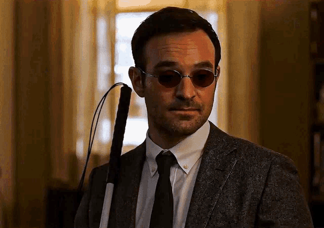 a man wearing sunglasses and a suit holds a cane