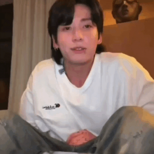 A man sits on the floor in a white shirt looking stunned at the camera.