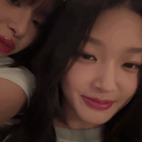 Two young women pose for a close selfie, with one smiling faintly.