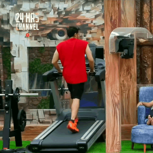 a man in a red shirt is running on a treadmill in front of a wall that says 24 hrs channel
