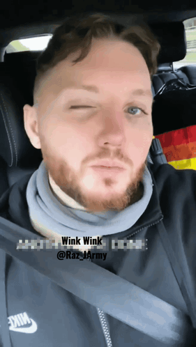 a man with a beard wearing a nike jacket is sitting in a car