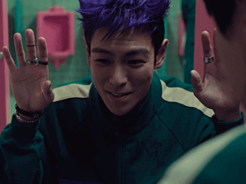 a man with purple hair and rings on his fingers looks at himself in a mirror