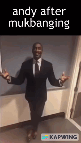 a man in a suit and tie is standing in a hallway with his arms outstretched and says andy after mukbanging