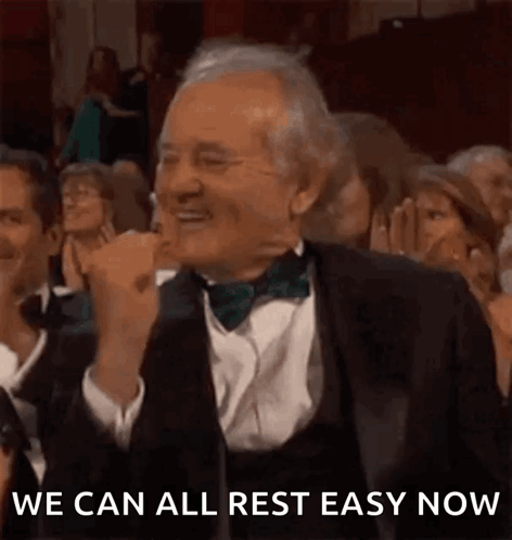 a man in a tuxedo and bow tie is sitting in a crowd of people and laughing .
