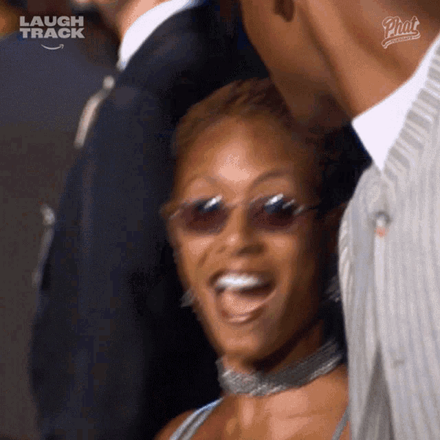 a woman wearing sunglasses and a choker is laughing with a laugh track logo in the background