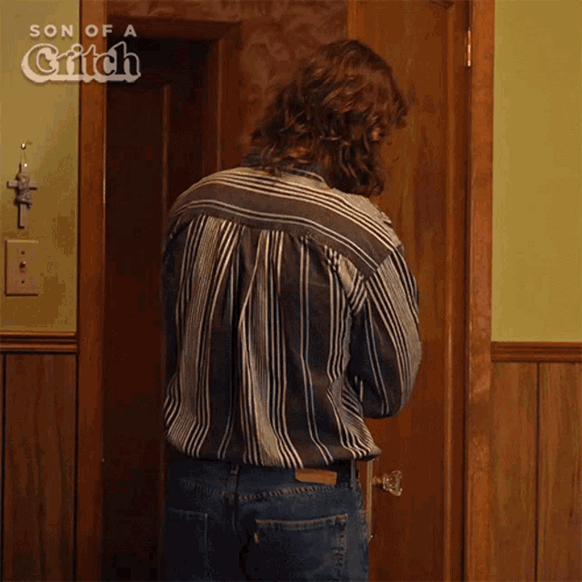 a man in a striped shirt is standing in front of a door that says son of a grifth