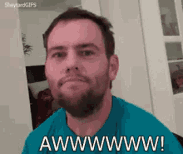 A bearded man in teal smiles bashfully beside “AWWWWWW!”