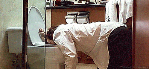 a man is bending over in front of a toilet .