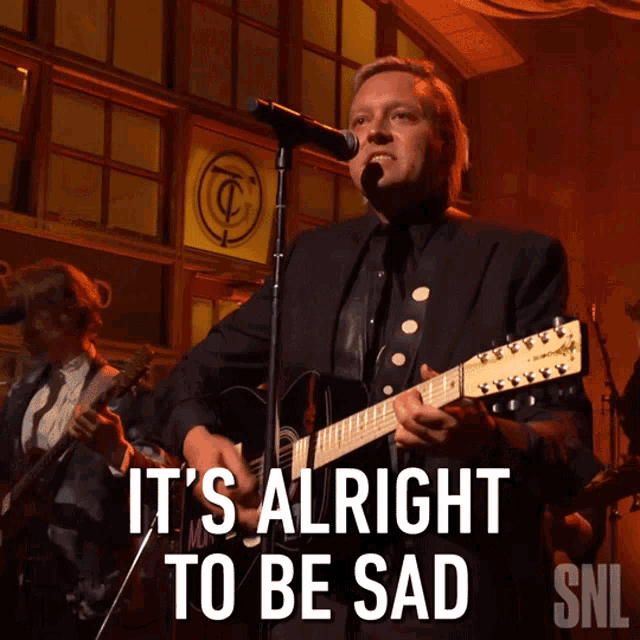 a man playing a guitar and singing into a microphone with the words it 's alright to be sad