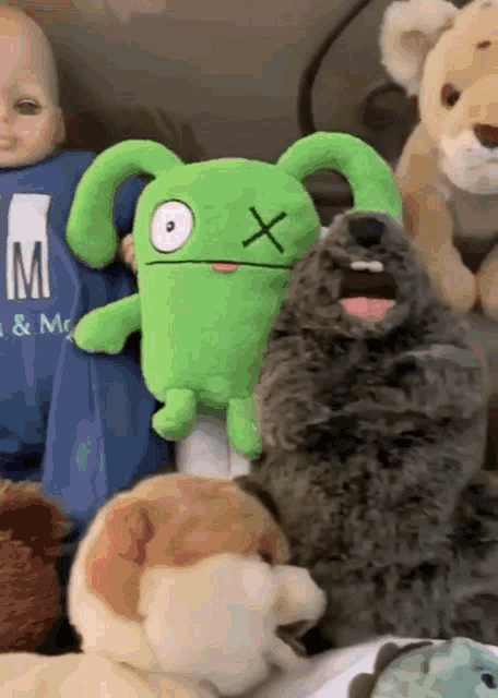 a green stuffed animal with an x on its eye is surrounded by other stuffed animals