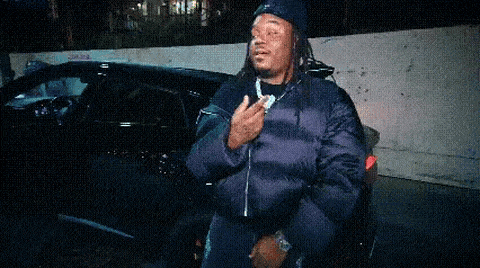a man with dreadlocks is standing in front of a car and giving the middle finger