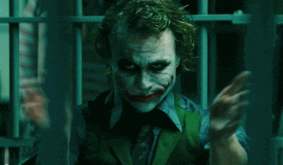 The Joker claps slowly in a dim green-lit room.