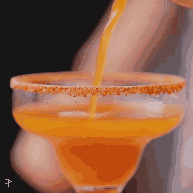 orange liquid is being poured into a margarita glass with a salt rim