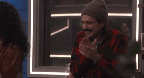 a man wearing a plaid shirt and beanie is clapping his hands