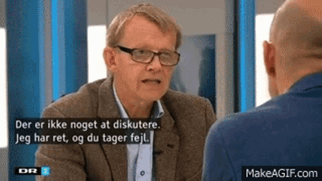 a man in a suit and glasses is talking to another man in a blue suit .