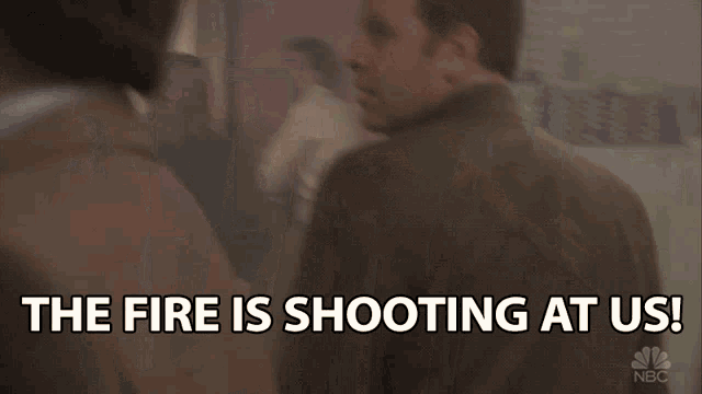 a man in a suit says " the fire is shooting at us " in front of a green exit sign