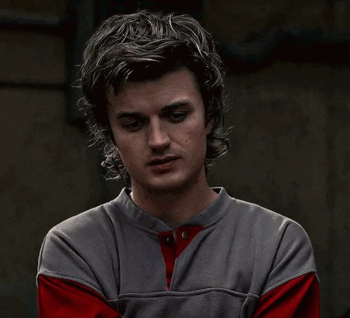 Steve Harrington looks stressed and overwhelmed in a dark room.