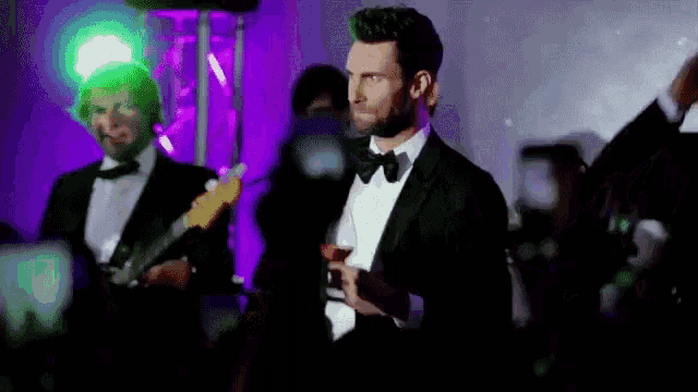 a man in a tuxedo is standing in front of a group of people .