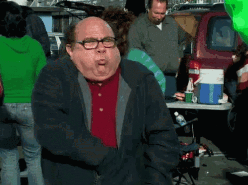 a man with glasses and a red shirt is standing in front of a table with a cooler on it .