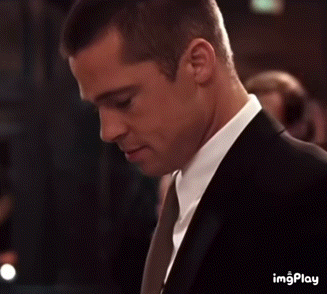 A man in a suit looks down with a coy expression.