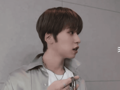 a young man wearing a white shirt and a necklace looks to the side