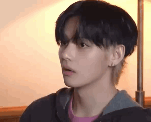 a close up of a young man wearing a hoodie and earrings looking at the camera .