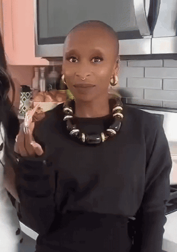 a woman with a shaved head wearing a black sweater and a black necklace