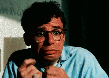 A bespectacled man recoils in terror while holding up his hands.