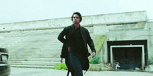 a man is running in front of a building with stairs and a car in the background .