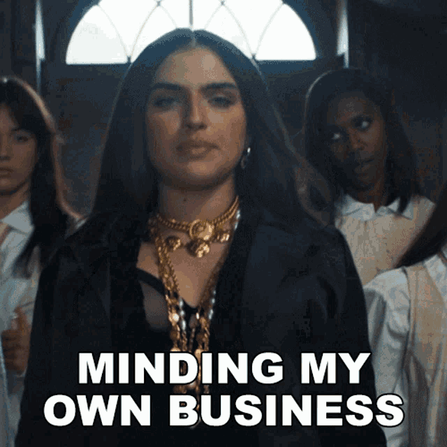 a woman in a black jacket stands in front of a group of girls with the words minding my own business above her