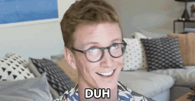 a man wearing glasses is smiling and has the word duh on his neck