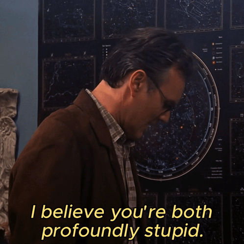 a man wearing glasses stands in front of a poster that says i believe you 're both profoundly stupid
