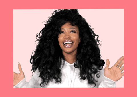 SZA smiles warmly with her hands raised in celebration.
