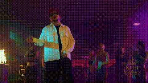a man wearing sunglasses and a hat is standing in front of a building with a fire in the background .