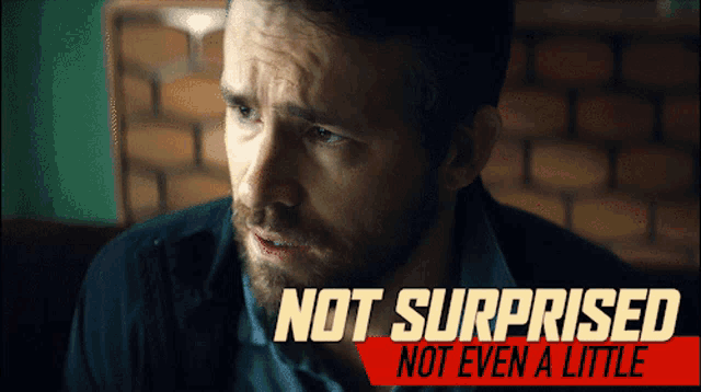 a man with a beard is sitting in front of a sign that says not surprised