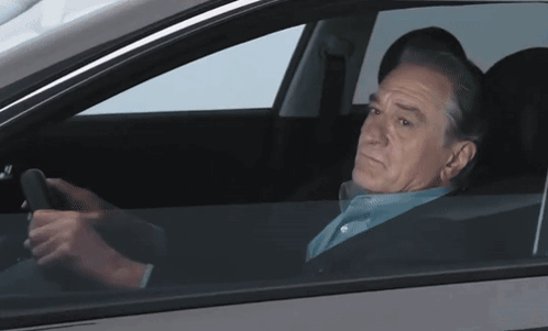 a man in a blue shirt is driving a car and looking out the window